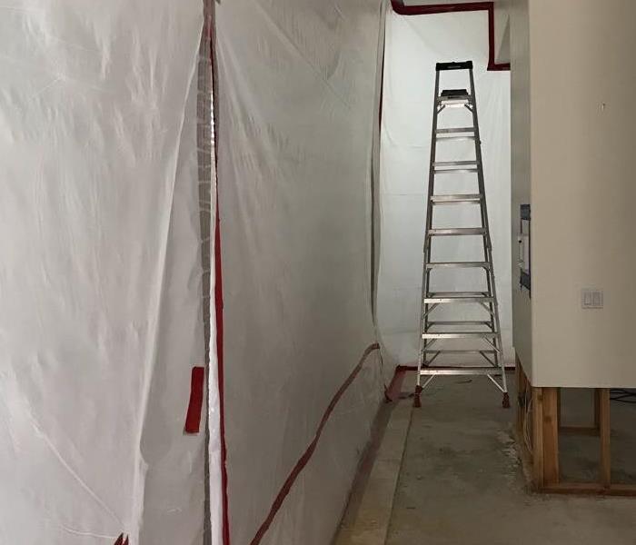 Hallway with plastic wrap on the walls and a ladder at the end.